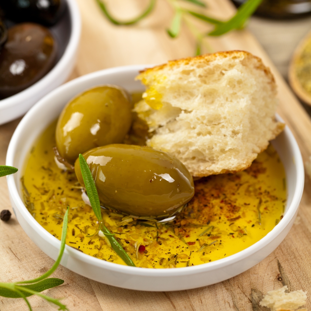 Weißbrot mit zwei Oliven liegen in Olivenöl in weißer Schale